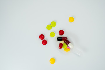 Colorful tablets in teaspoon and many pills spread on a white background