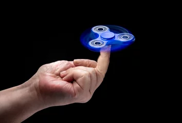 Foto auf Leinwand Spinning fidget spinnet toy in human left hand isolated on black background. Super popular device. © Leo Zank