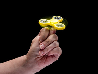 Spinning fidget spinnet toy in human left hand isolated on black background. Super popular device.