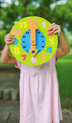 Little child girl showing up 6 O'clock round toy clock in the garden.