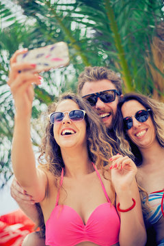 Friends taking selfie at beach, palm tree at background