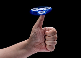 Spinning fidget spinnet toy in human left hand isolated on black background. Super popular device.