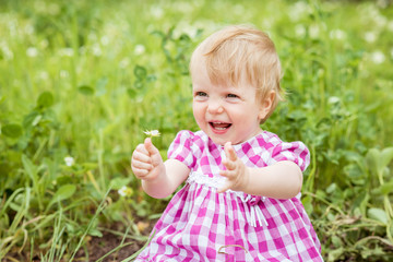 Portrait of a beautiful baby girl sitting on green meadow