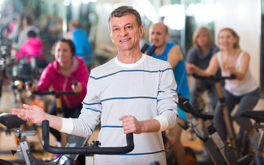 Fototapeta na wymiar Elderly man on fitness cycle in fitness club.