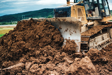 yellow mini bulldozer working with earth and soil while doing landscaping works on construction site