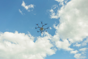 Fototapeta na wymiar Hovering drone flies in blue sky and taking pictures of green hills. Professional agriculture drone flying in clear blue. Sky partly clouded