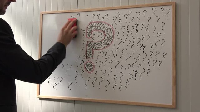 Businessman erasing question marks on office whiteboard during business seminar presentation, leaving one large symbol for big question