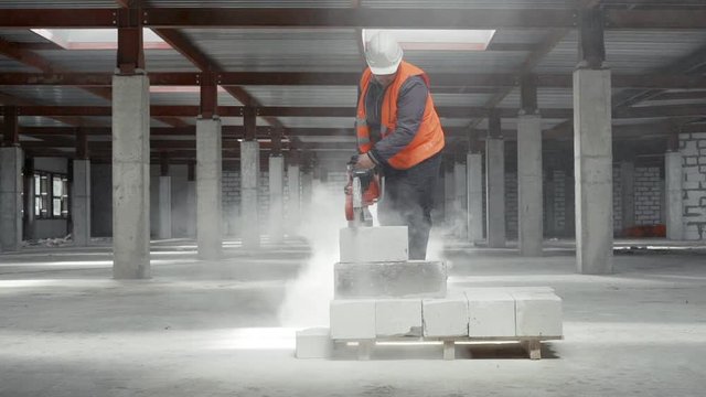 A worker at the construction site saws circular saws concrete block