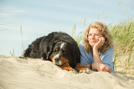 mature woman with her dog on sand and grass sitting