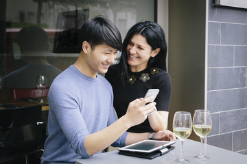 Multiethnic couple in a restaurant looking at phone with a glass of white wine