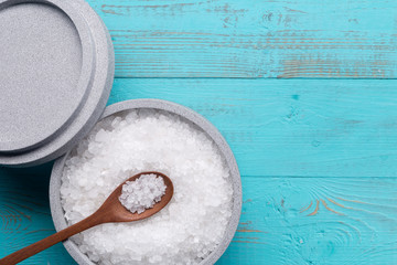 Sea salt in an stone bowl with small wooden spoon on a blue wooden table