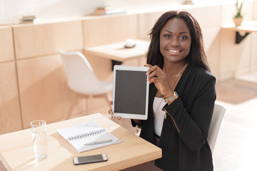 smiling african american woman presenting digital tablet with blank screen while sitting in cafe