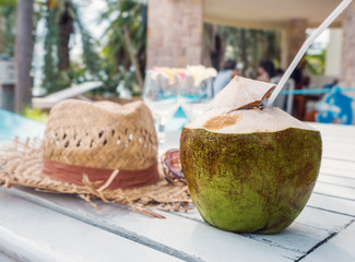 Coconut water on white wooden table, against blurred beach accessories background in sunny day.