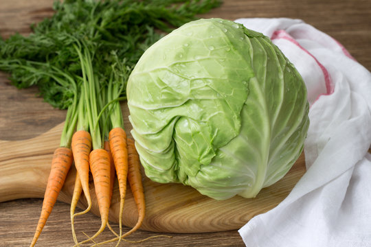 Fresh young cabbage and carrots with greens for coleslaw salad on a wooden board on a wooden table, selective focus. Healthy diet food