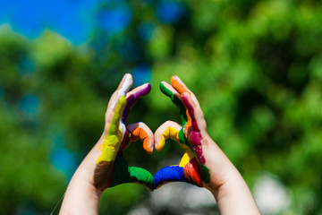 Kids hands painted in bright colors make a heart shape on summer nature background. Art and painting concept