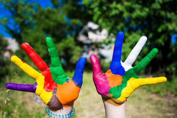 Child hands painted in bright colors isolated on summer nature background. Art and painitng concept