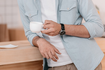 close-up partial view of young man holding white cup and drinking coffee