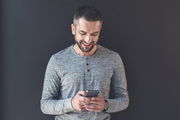 Delightful manager male is holding smartphone with smile