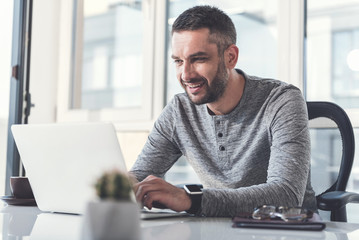 Cheerful man with stubble is typing on modern gadget