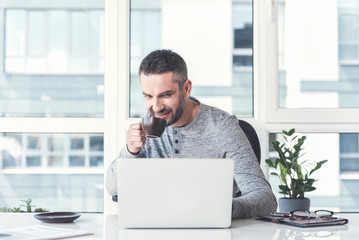 Obraz premium Joyful confident businessman is enjoying espresso doing his job