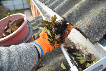 Rain Gutter Cleaning from Leaves in Autumn with hand. Roof Gutter Cleaning Tips. Clean Your Gutters...