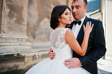 Amazing young attractive newly married couple walking and posing in the downtown with beautiful and ancient architecture on the background on their wedding day.