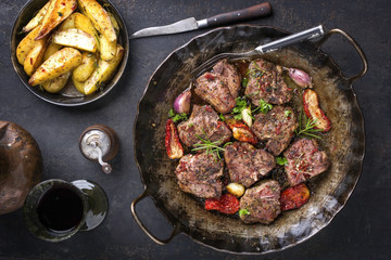 Barbecue T-bone lamb steak with fried potatoes and seasonings as top view in an iron cast pan © HLPhoto