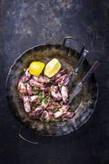 Fried octopus with lemon slices as top view in an iron pan