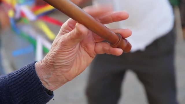 Detalle de manos de musico, tocando musica tradicional de flauta y tambor, y gente bailando al fondo