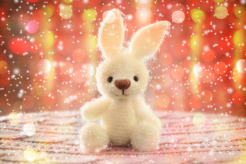 Knitted toy bunny on Christmas lights background. Holidays celebration concept