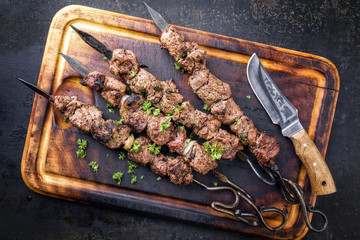 Traditional Russian shashlik on a barbecue skewer as top view on an old burnt cutting board