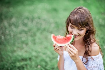 Young beautiful woman sitting on the grass and eat watermelon. Happy girl resting on the grass. Warm summers. Watermelon.