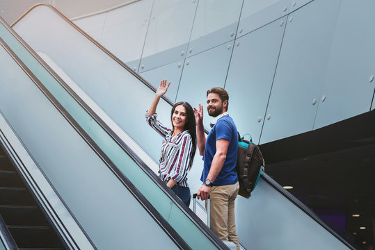 Pleasant couple is standing on escalator with suitcase