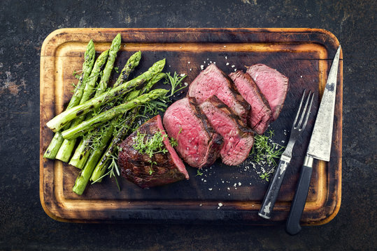 Barbecue Wagyu H&uuml;ftsteak mit gr&uuml;nen Spagel als close-up auf verbrannten Schneidebrett