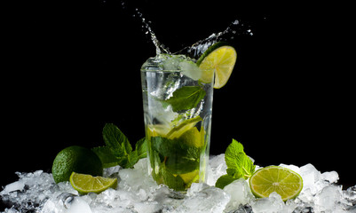 Mojito, a cool cocktail of lime and mint and soda, in a highball glass with a splash and ice, isolated on a black background