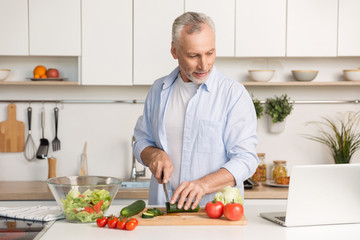 Fototapeta premium Handsome man standing at the kitchen using laptop and cooking