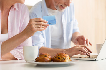 Cropped of mature loving couple using laptop holding credit card