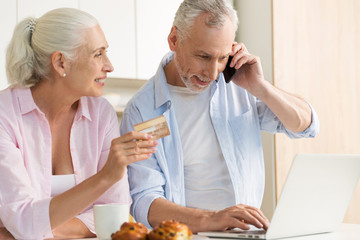 Smiling mature loving couple family using laptop holding credit card.