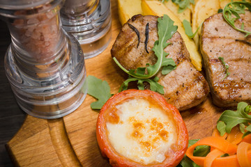 Three pork steaks with fried potatoes and vegetables on a wooden background