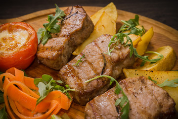 Three pork steaks with fried potatoes and vegetables on a wooden background