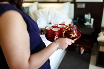 Woman holds red tray with Asian teapot and red cups