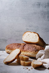 Homemade white wheat bread whole and slice served with flour and wheat grain seeds, white linen towel over gray texture kitchen table.