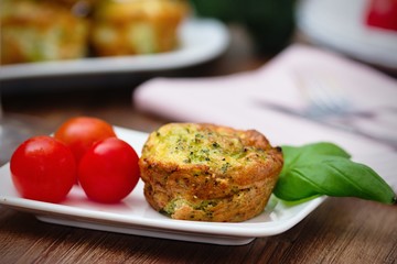 Broccoli savory cake served with cherry tomatoes and leaves of basil on white plate on a wooden table