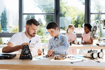 Pre-teen boy and his teacher connecting wires of robot