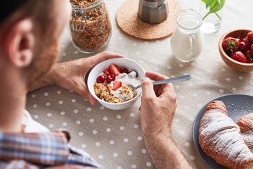 Man eating muesli with yogurt and fresh berries by breakfast