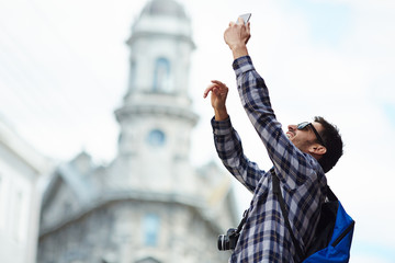 Fototapeta premium Portrait of modern young tourist on solo trip in Europe, happy man taking selfie photo in street of old city
