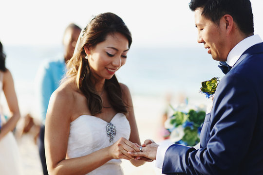 Bride puts a ring on groom's finger standing on the beach