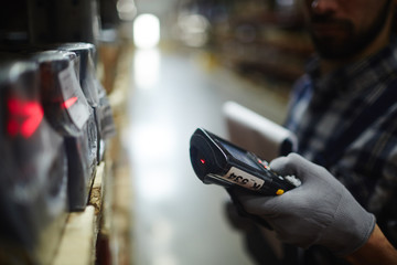 Side view closeup of bar code scanner in hand of unrecognizable warehouse worker doing inventory of stock