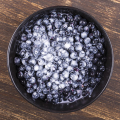 Fresh, ripe forest blueberries with sour cream in black plate.
