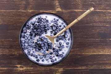 Fresh, ripe forest blueberries with sour cream and honey in black plate.